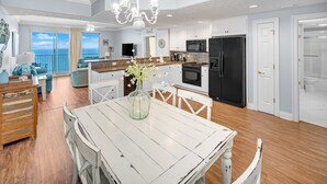 A spacious living area with a dining table, white walls, and a view of the ocean. - Beachfront condo w/ pool, hot tub & gym (Panama City Beach)
