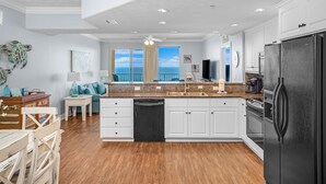 A modern kitchen with white cabinets, a black refrigerator, and a dining area with a wooden table and chairs. - Beachfront condo w/ pool, hot tub & gym (Panama City Beach)