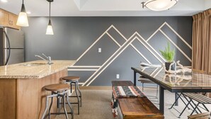 Une cuisine moderne dotée d’un coin bar, de tabourets de bar, d’une table à manger avec des bancs et d’un éclairage suspendu.