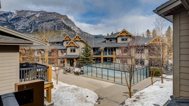 Un quartier résidentiel composé de plusieurs maisons, dont l’architecture est un mélange de styles modernes et traditionnels, avec une piscine et un paysage montagneux en toile de fond.