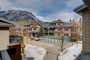 A residential area with multiple houses featuring a mix of modern and traditional architecture, a swimming pool, and a mountainous backdrop. - Your Lovely 3BR/2BA Condo at the Edge of Canmore (Dead Man`s Flats)