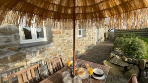 Una mesa de madera con un dosel de paja, paredes de piedra y un camino empedrado.