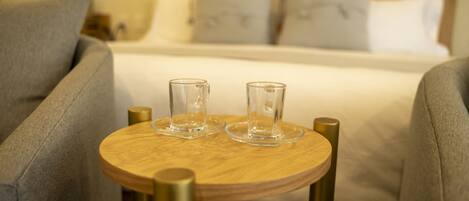 A neatly arranged bedroom with a bed, two bedside tables, and a small wooden table with two glasses.