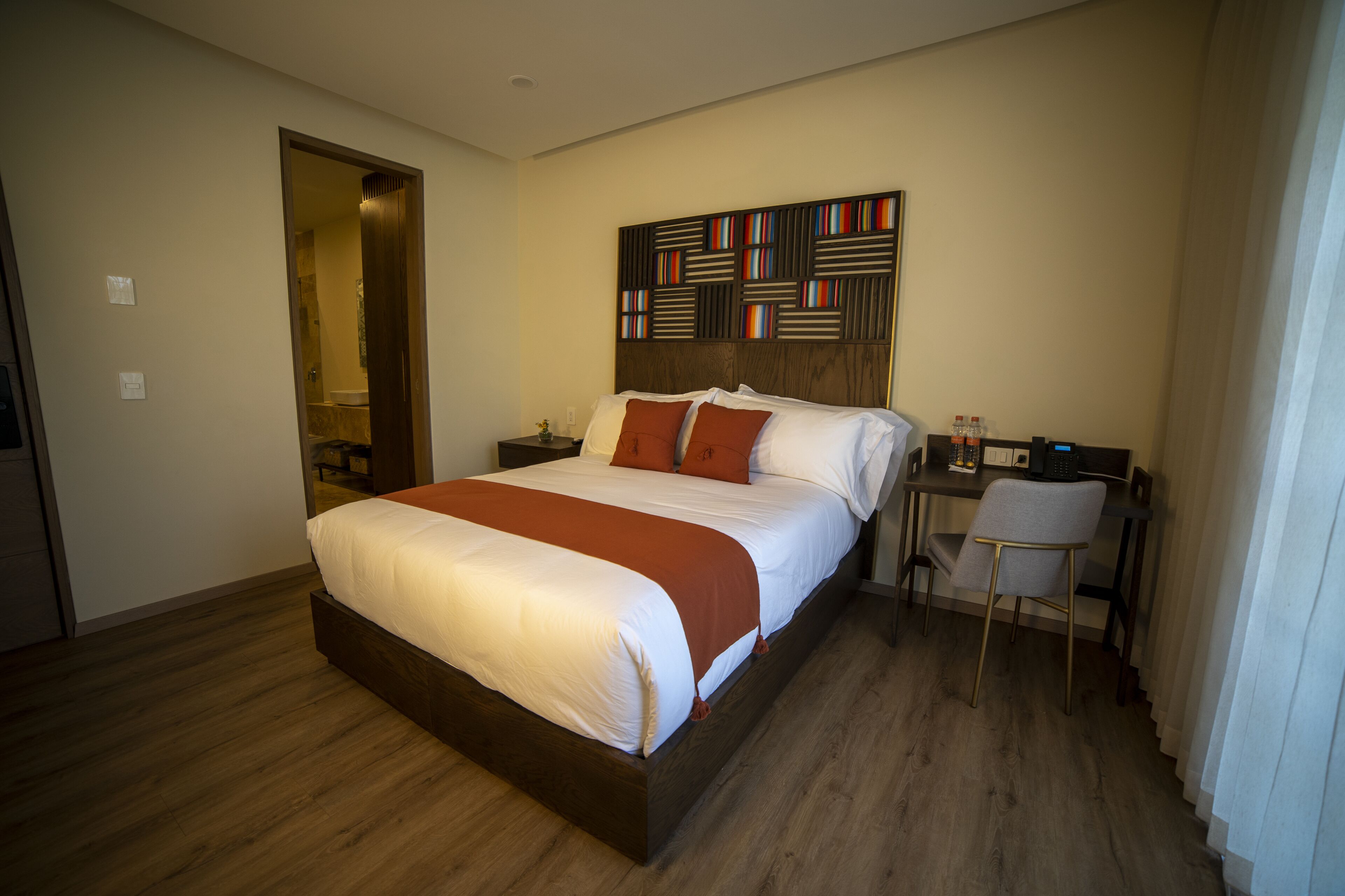 A hotel room with a large bed, a desk with a chair, and a wall-mounted artwork.