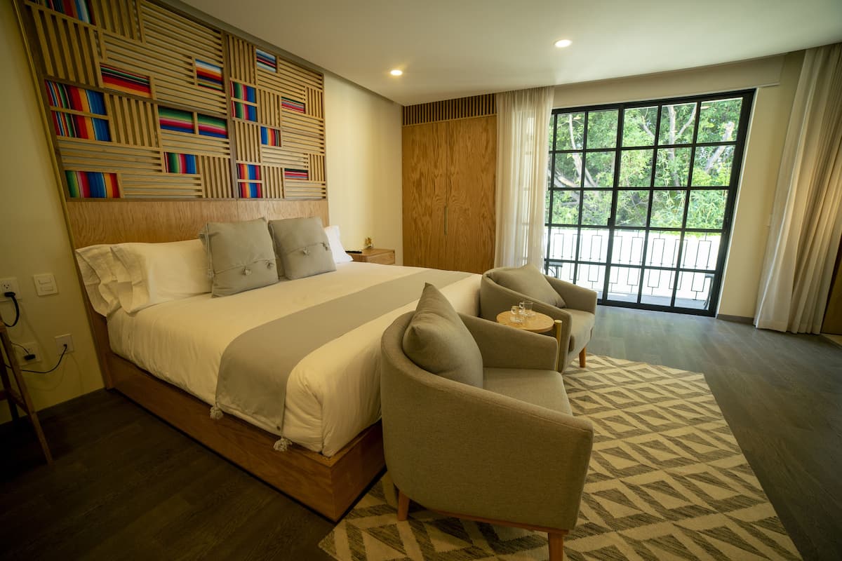 Un dormitorio moderno con una cama grande, un sofá y un ventanal con vistas a árboles.