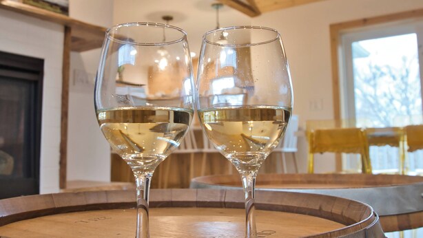 Two wine glasses on a round metal table in a room with wooden beams and a large window.