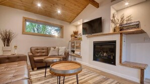 A cozy living room with leather sofas, a fireplace, and a television mounted on the wall.