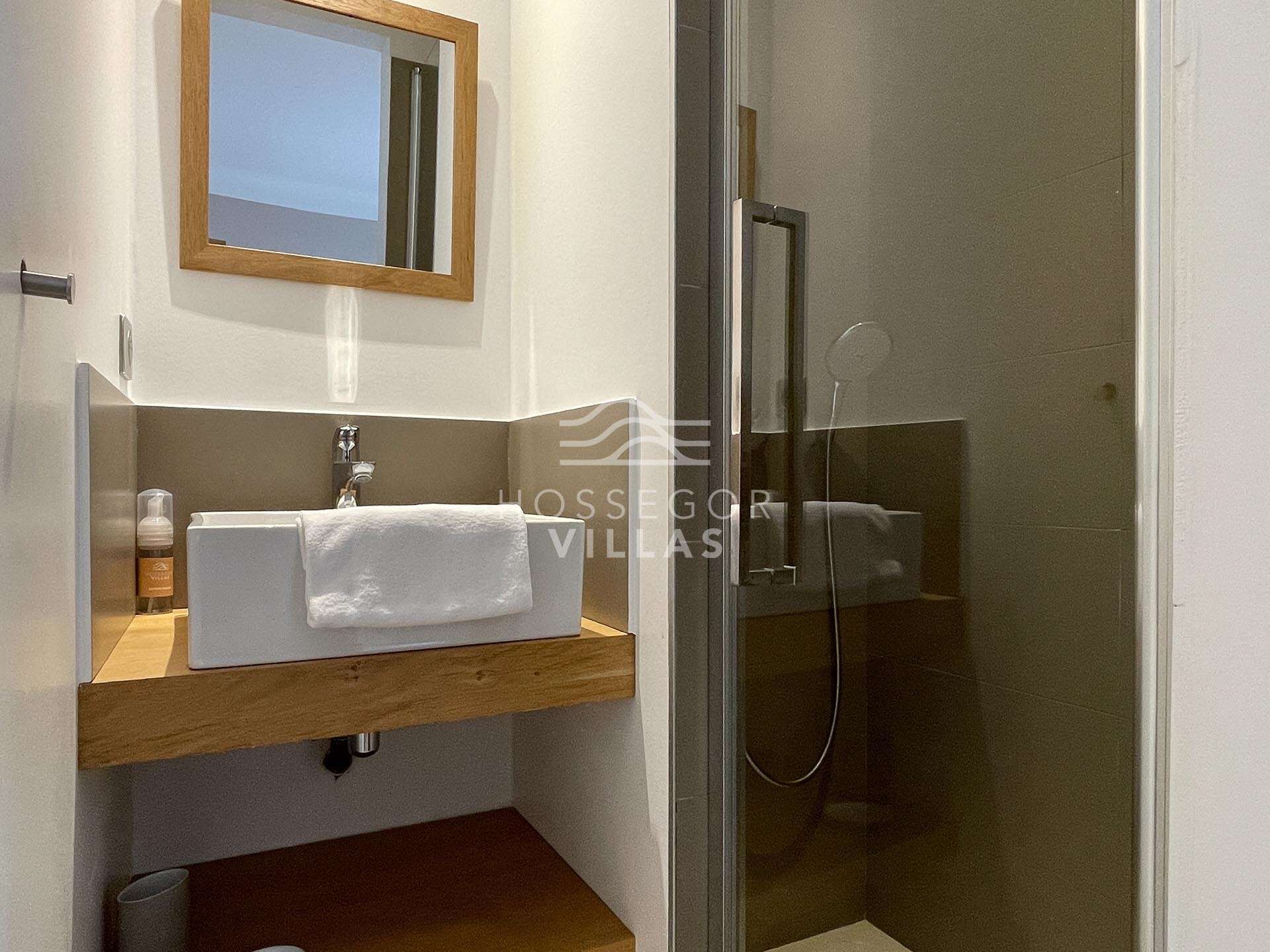 A modern bathroom with a wooden vanity, a white sink, and a glass shower enclosure.