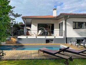 Ein modernes, zweistöckiges Haus mit Swimmingpool, Sitzgelegenheiten im Freien und einem Garten.