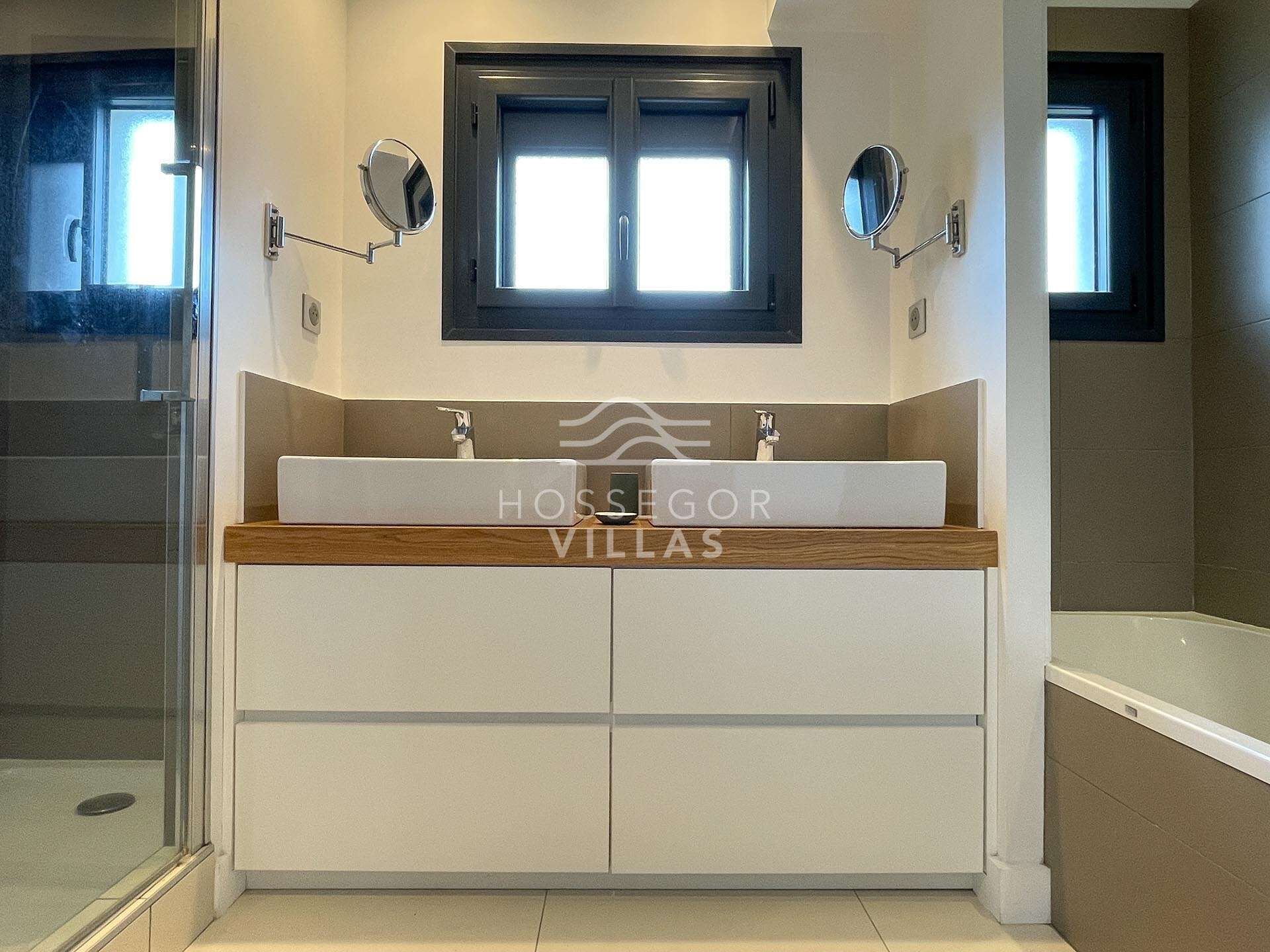 A bathroom with a double sink, a window above the sink, and a mirror on the wall.