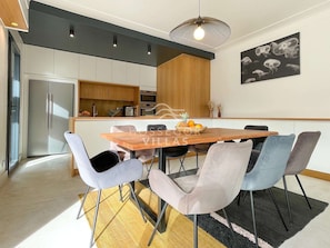 A modern kitchen with a wooden dining table, light-colored chairs, and a black and white artwork on the wall.