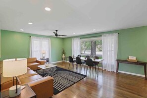 Un salon comprenant un canapé, une table basse, une table à manger avec des chaises, un ventilateur de plafond et une vue sur l’extérieur grâce à de grandes fenêtres.