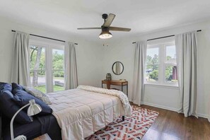 Une chambre à coucher avec un lit, un bureau, un ventilateur de plafond et de grandes fenêtres.