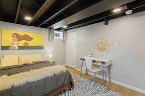 A bedroom with a bed, a desk, a chair, a painting, and a door.