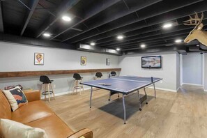 A room with a ping pong table, leather sofa, and chairs.
