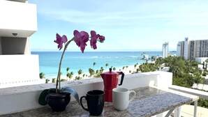 Een balkon met uitzicht op de oceaan, een pot orchidee en twee koffiekopjes.