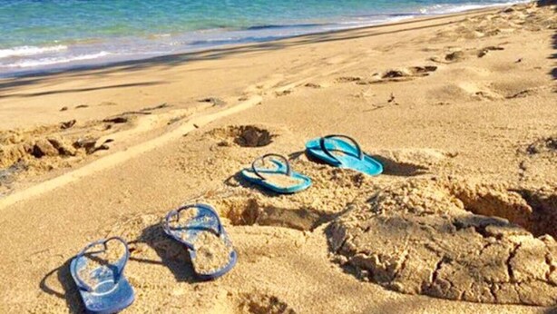 Een strand met voetafdrukken en slippers in het zand.