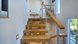 A modern staircase with wooden steps and metal railings, leading to a balcony with a view of greenery. - Luxury Home | Large Outdoor Patio & Dining | BBQ (Encinitas)