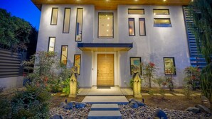 A modern two-story house with a wooden front door, multiple windows, and a well-lit entrance. - Luxury Home | Large Outdoor Patio & Dining | BBQ (Encinitas)