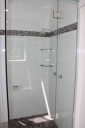 Een douche met glazen wanden, een betegelde vloer en een klein plankje.