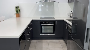 Een moderne keuken met een centraal kookeiland, een inbouwoven, roestvrijstalen apparatuur en een potplant.