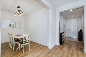 Ein Essbereich mit einem Holztisch und Stühlen, einer hängenden Leuchte und einer weißen Tür im Hintergrund.