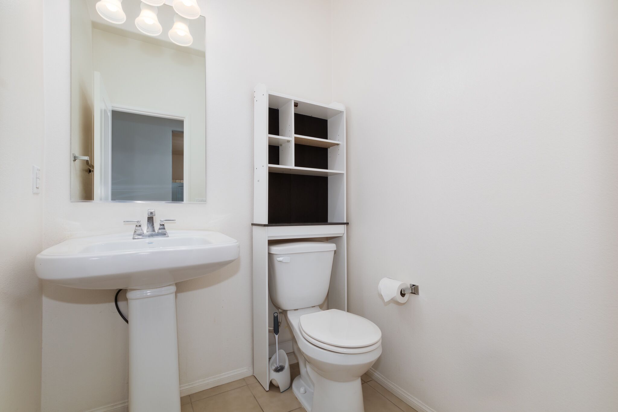 Une salle de bain avec un lavabo blanc, des toilettes et une étagère ouverte.