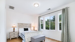 A bedroom with a wooden bed, bedside lamps, a bench, and a large window with curtains.