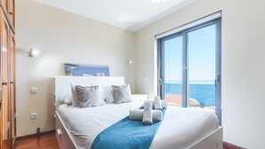A bedroom with a bed, a blue blanket, and a view of the sea through a large window. - Dream House by Atlantic Holiday (Ponta Delgada)