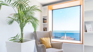 A modern living room with a large window, a grey armchair, a white side table, and a potted plant. - Dream House by Atlantic Holiday (Ponta Delgada)
