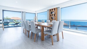 A modern dining area with a wooden table and chairs, large windows, and a view of the sea. - Dream House by Atlantic Holiday (Ponta Delgada)