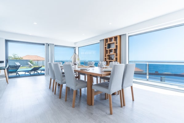 A dining area with a wooden table, grey chairs, and a view of the sea.