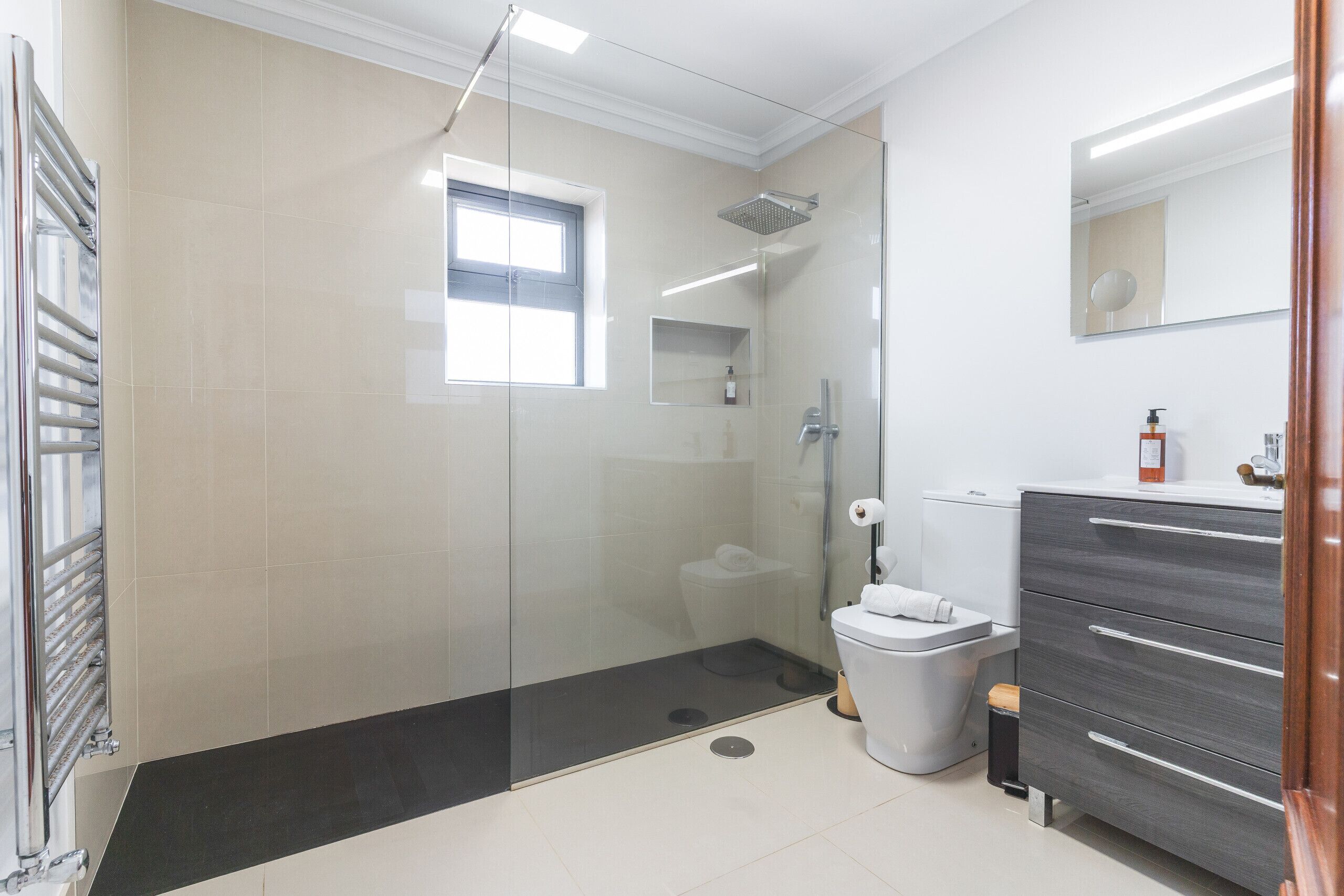 Une salle de bain moderne avec une douche à parois de verre, des toilettes, un meuble-lavabo avec des tiroirs et un miroir.