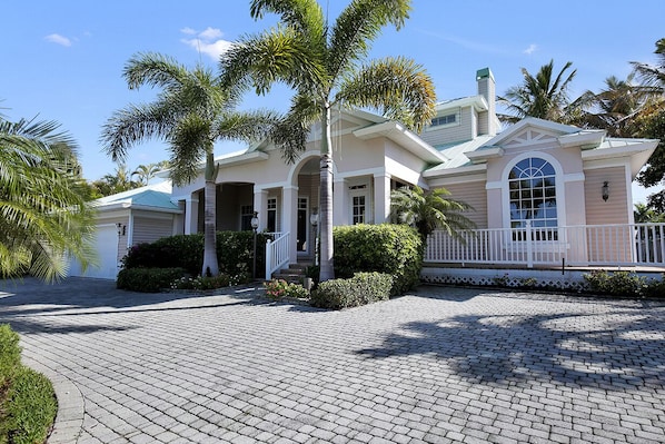 A two-story house with a covered front porch, a brick driveway, and palm trees. - Enjoying paradise on Marco Island with direct access! (Marco Island)