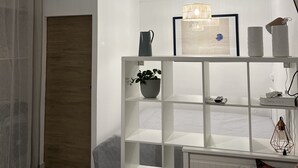 Un dormitorio moderno con una cama blanca, un estante blanco, una planta en maceta, un cuadro enmarcado y una lámpara colgante.