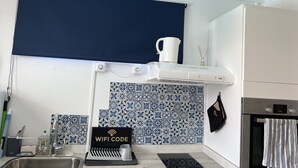 Una cocina moderna con salpicadero de azulejos azules y blancos, un lavamanos de acero inoxidable, una campana extractora blanca y un cartel con un código WiFi.