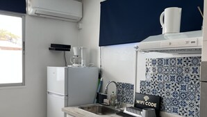 Una cocina compacta con refrigerador integrado, cafetera, lavamanos y salpicadero con azulejos azules y blancos.