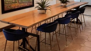 Un comedor con una larga mesa de madera, sillas azules, plantas en macetas y dos candelabros.