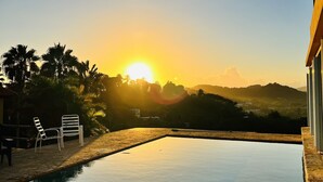 Una piscina con sillas de descanso y vista al atardecer sobre un paisaje montañoso.