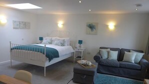 A bedroom with a bed, bedside tables, a grey sofa, a small ottoman, and a desk. - The Rock Self Catering Holiday Accommodation (Coleford)