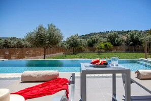 A poolside area with lounge chairs, a table with a fruit bowl and glasses, and a view of a hillside with trees. - Villa Alkistis in Lefkada (Lefkada)
