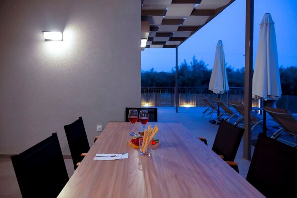 An outdoor dining area with a wooden table, chairs, and umbrellas. - Villa Alkistis in Lefkada (Lefkada)