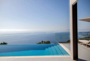 Ein moderner Infinity-Pool mit klarem, blauem Wasser, Blick aufs Meer und eine Lounge-Bereich mit einem weißen Sonnenschirm.