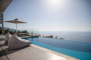 Ein Infinity-Pool mit freiem Blick auf das Meer, Liegestühle und ein Sonnenschirm.