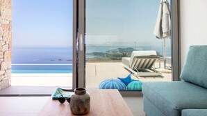 A modern living room with a view of the sea, a wooden table with a vase, and a blue sofa. - Syvota 03 Sunset 2B Isidora (Igoumenitsa)