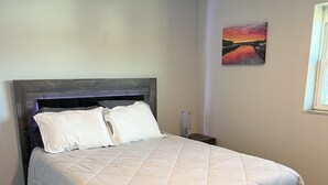 A bedroom with a dark wooden bed frame, white bedding, and a nightstand with a lamp. - Remodeled townhouse - 5 mins from Shawnee Sports Complex! (Dunbar)