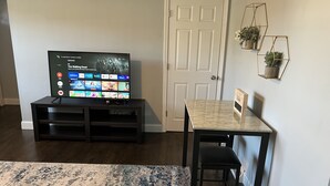 A living room with a flat-screen TV on a black stand, a marble table, a black chair, a wooden bench, and a patterned rug. - Remodeled townhouse - 5 mins from Shawnee Sports Complex! (Dunbar)