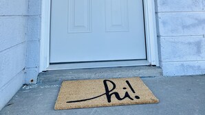 A white door with a semi-circular window above it, a doormat with the word "Hi!" on it, and a small black mailbox on the wall to the right. - Remodeled townhouse - 5 mins from Shawnee Sports Complex! (Dunbar)