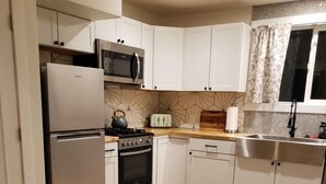 A compact kitchen with white cabinets, a stainless steel refrigerator, a microwave, a stove, and a sink.