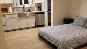 A bedroom with a bed, a small bedside table, and a nightstand. The room has wooden flooring and a window with curtains.